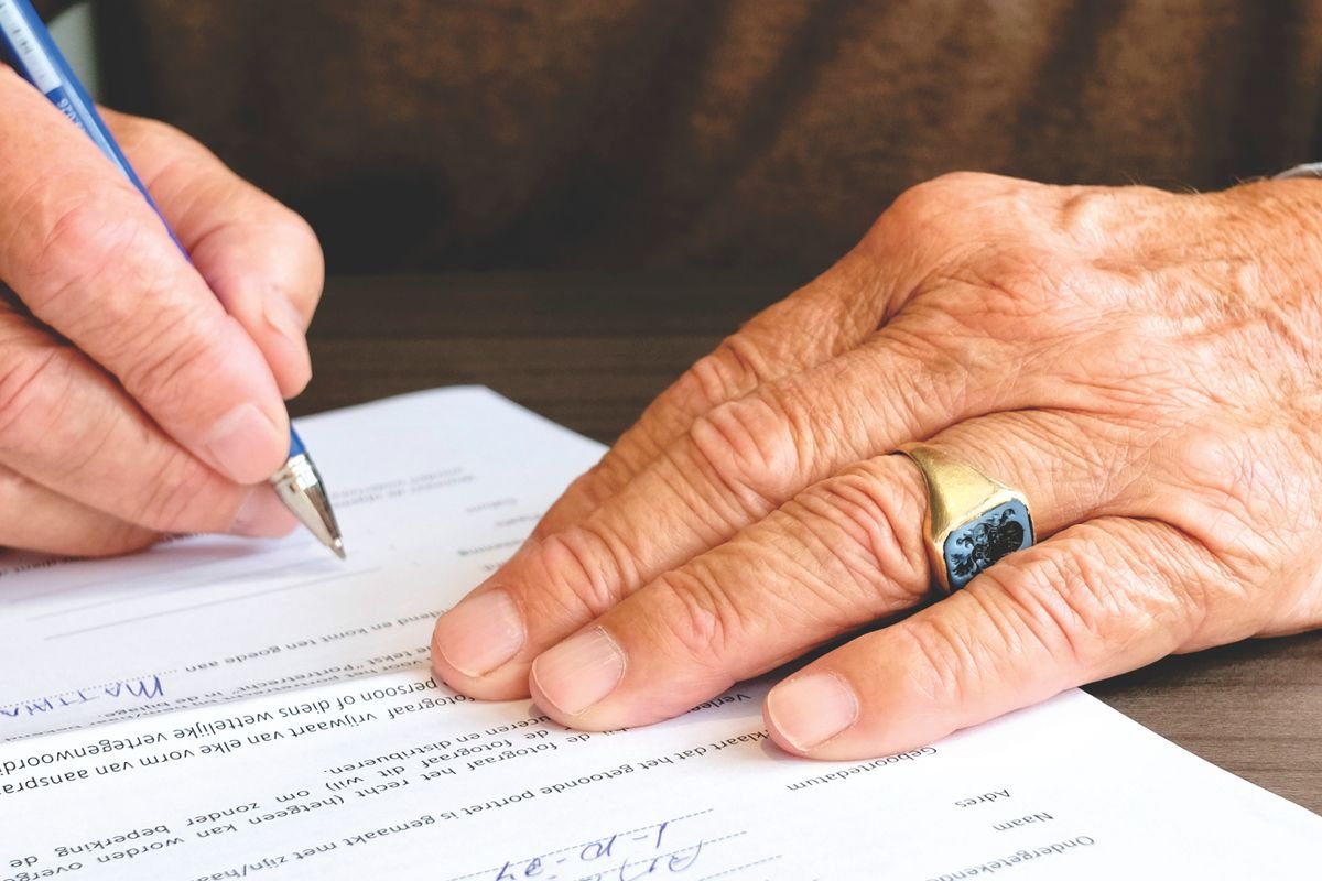 An older person signing a legal document, representing a will and estate planning for cryptoassets