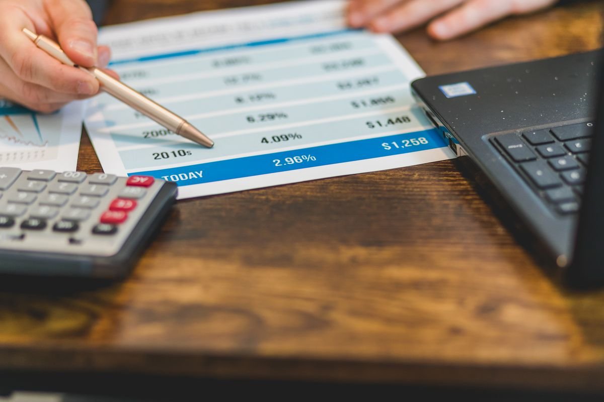 A hand annotating financial figures beside a calculator and laptop, representing an accountant checking a crypto computation before filing