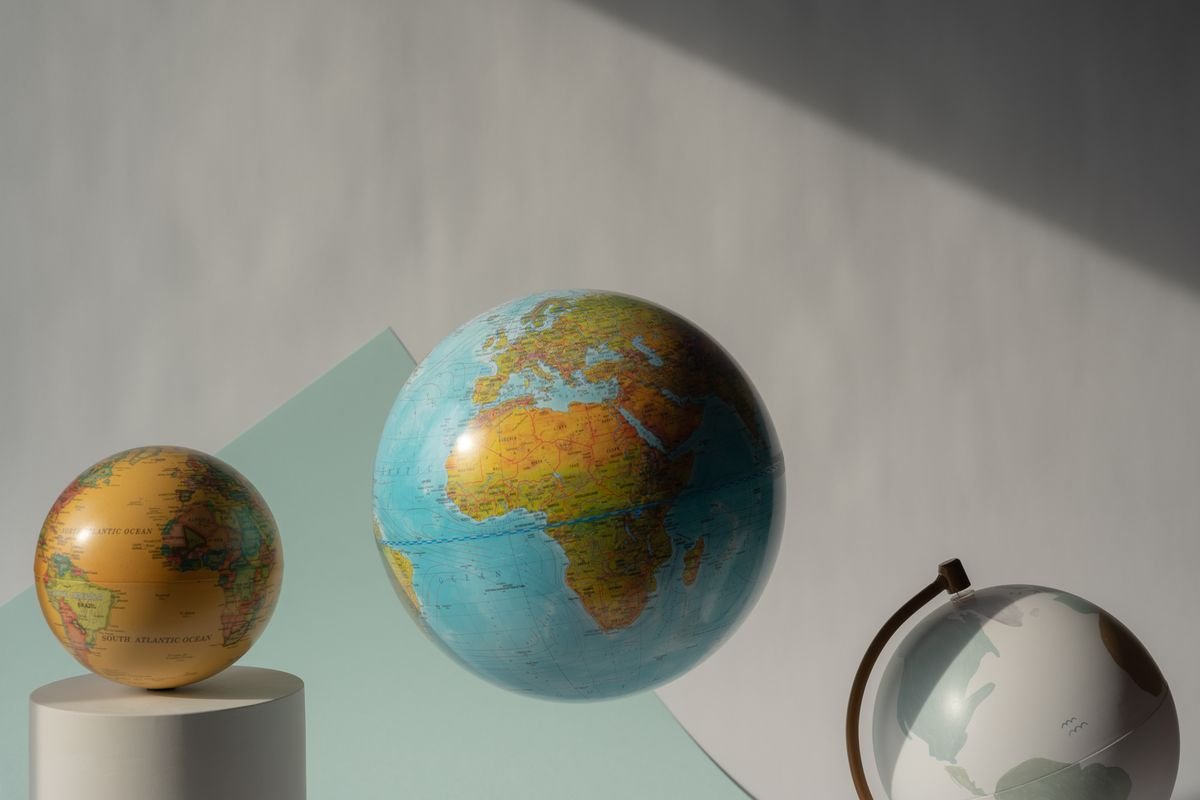 Three world globes on a studio background, representing crypto tax cost basis methods compared across jurisdictions