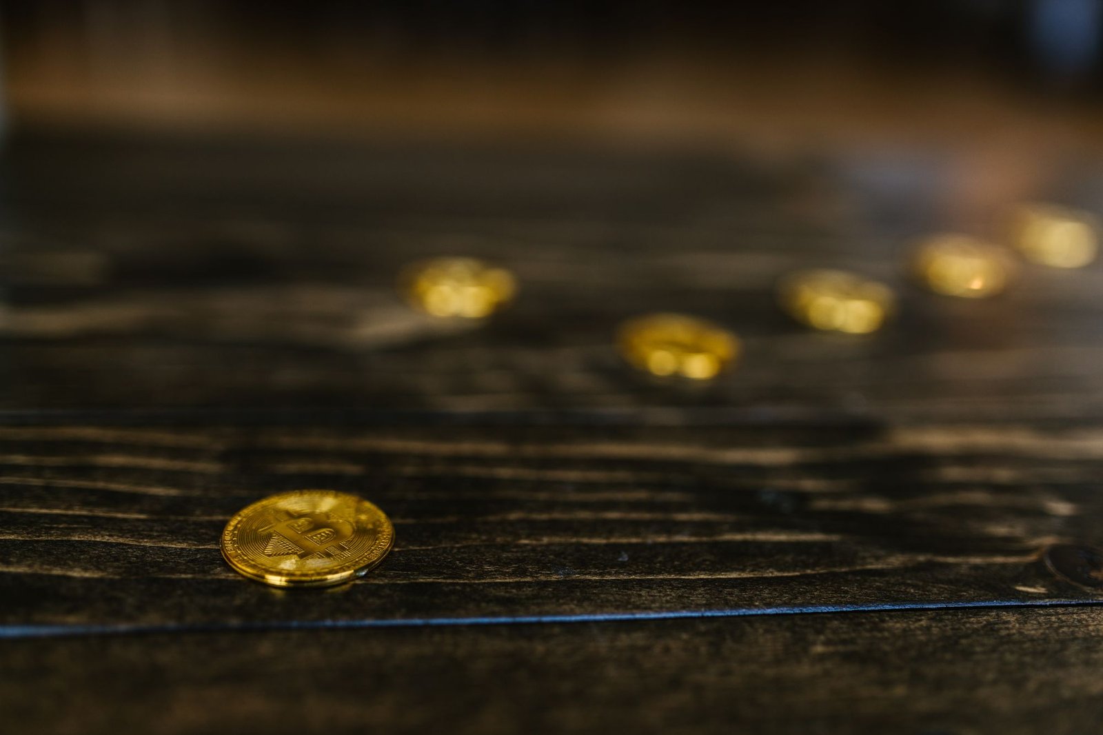 Gold Bitcoin coins scattered on a dark wooden surface, representing mined tokens