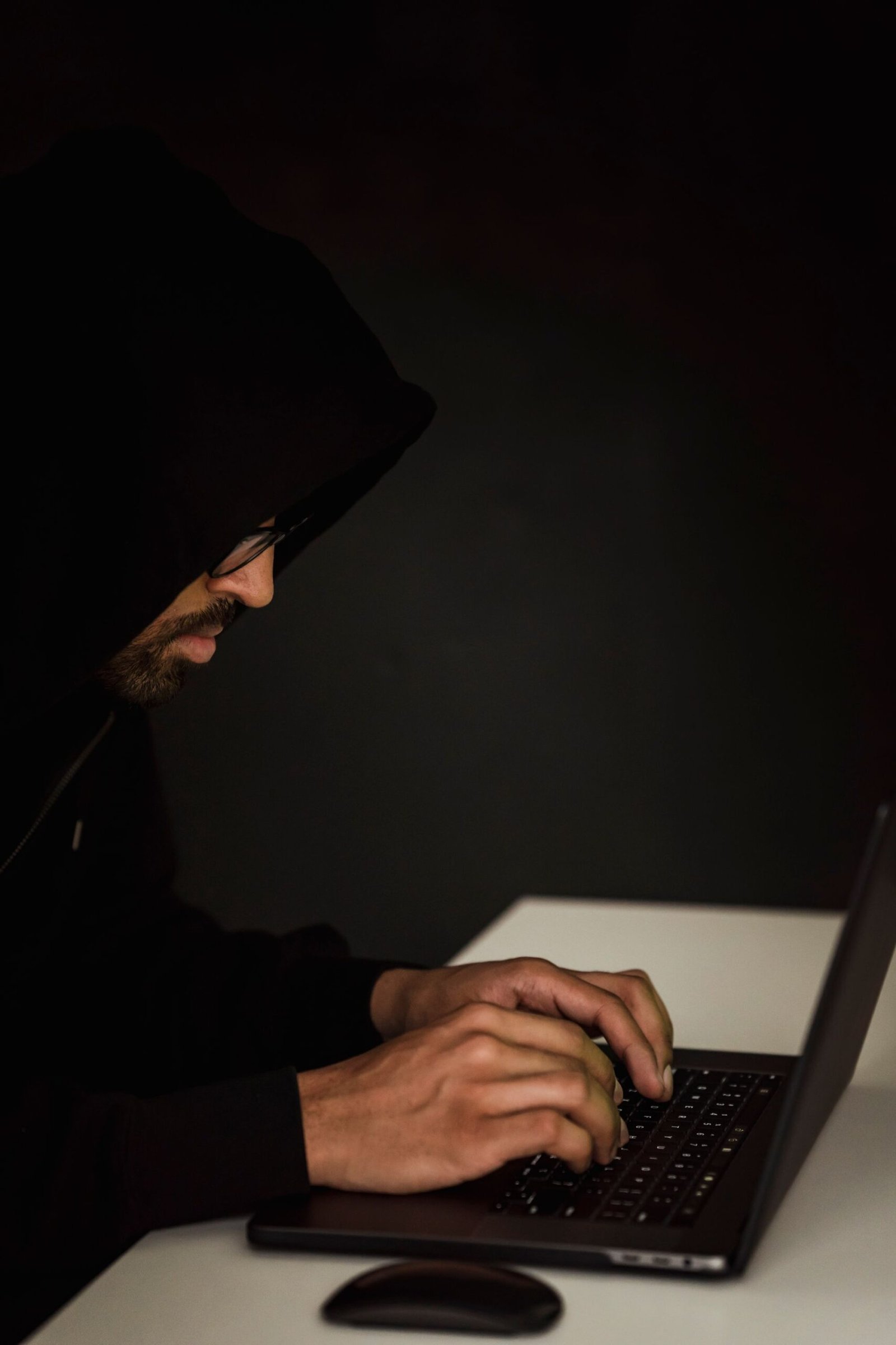 Low-lit figure at a laptop representing online cryptocurrency investment fraud
