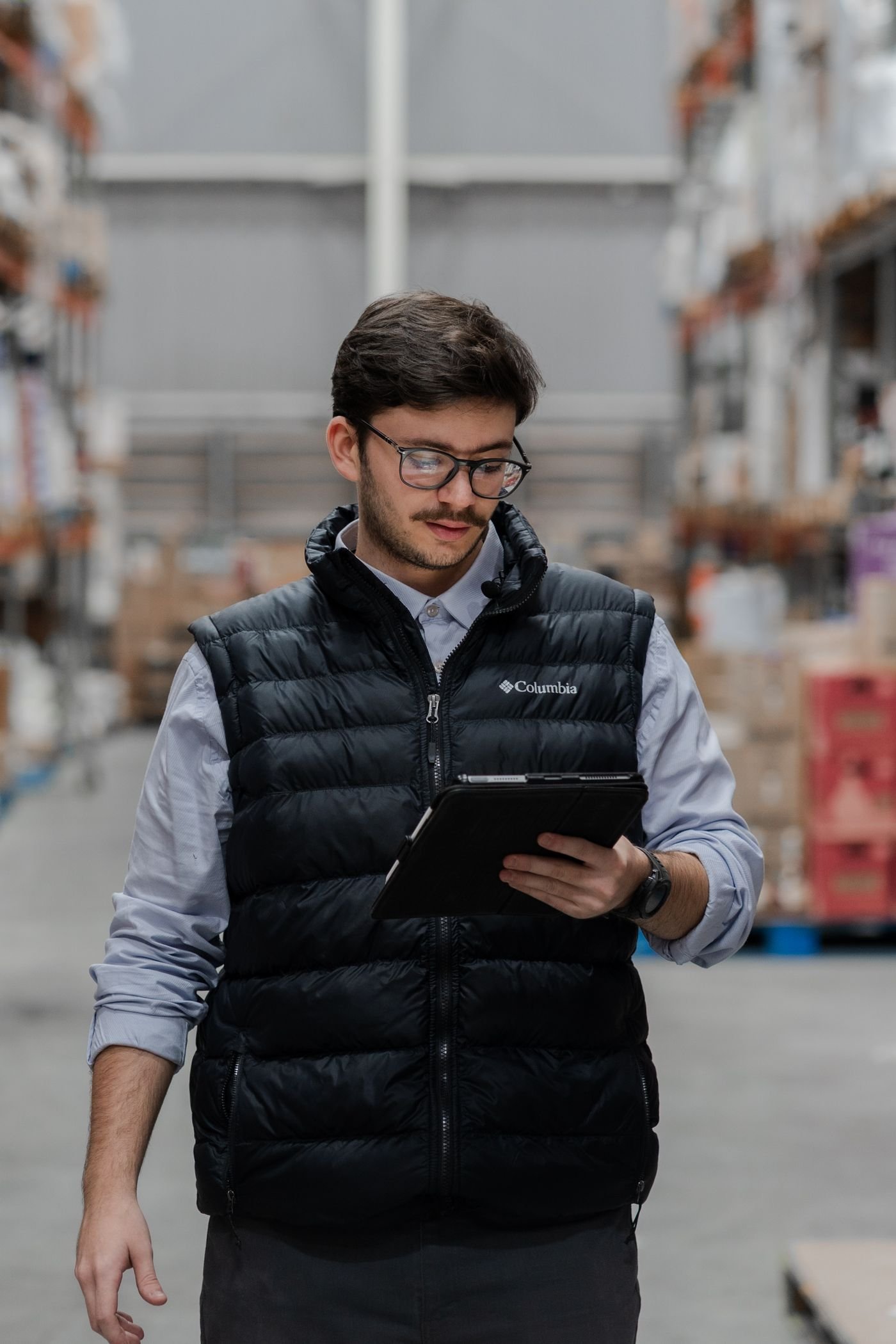 Warehouse operative checking stock levels on a tablet beside pallet racking