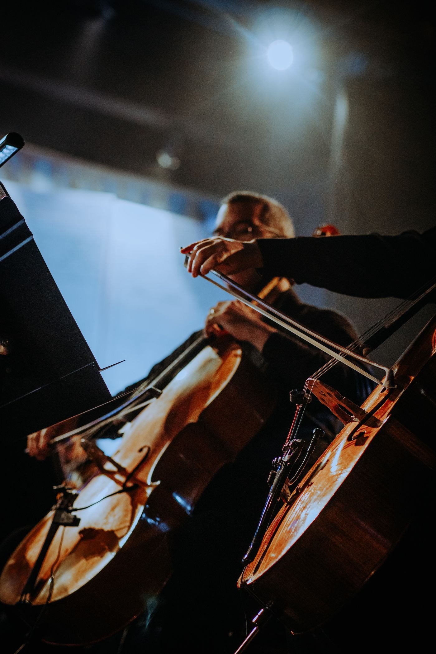 Cellist performing on stage with an orchestra under theatre lighting