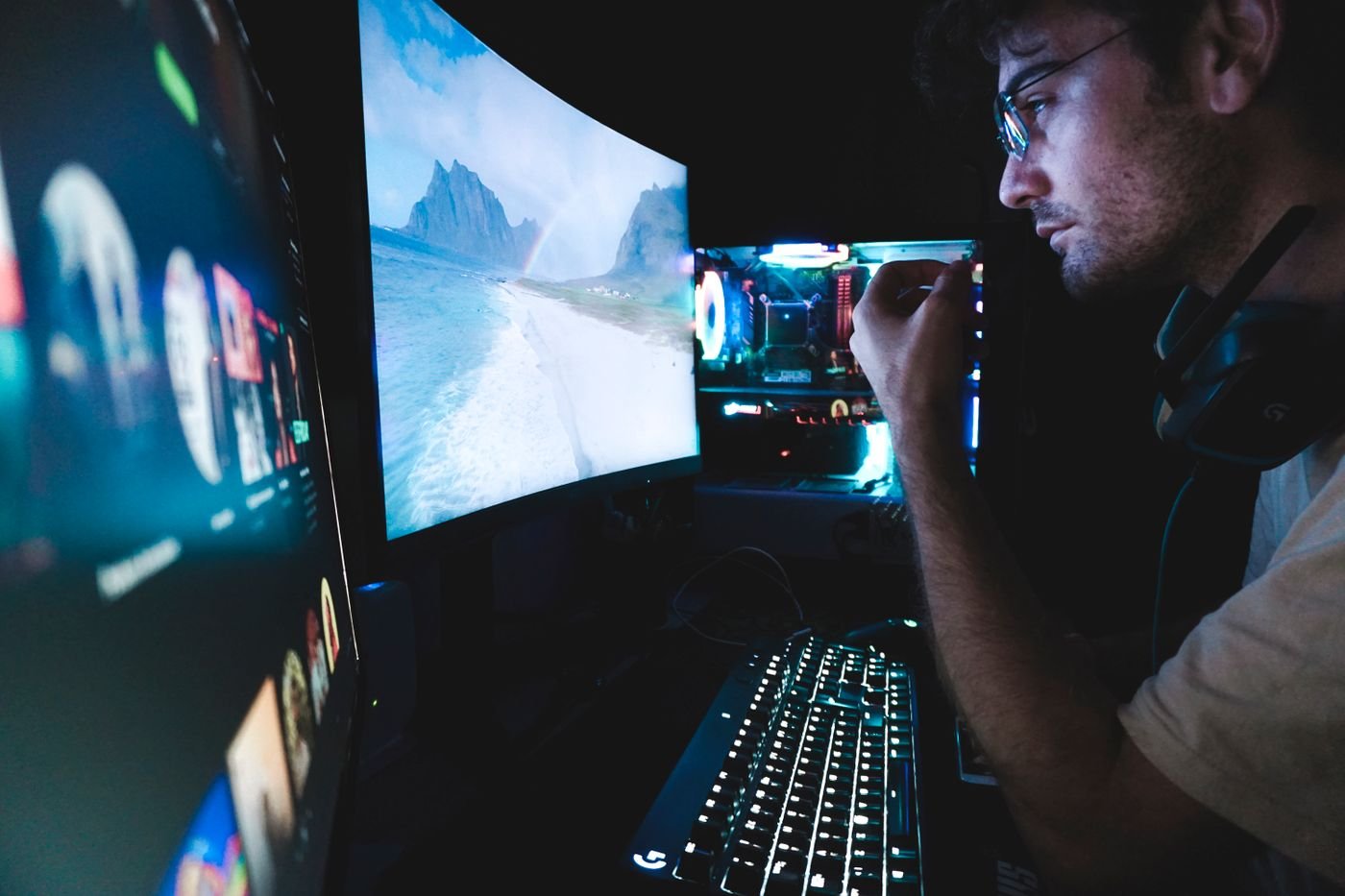 Games developer in glasses reviewing code on multiple monitors in a studio